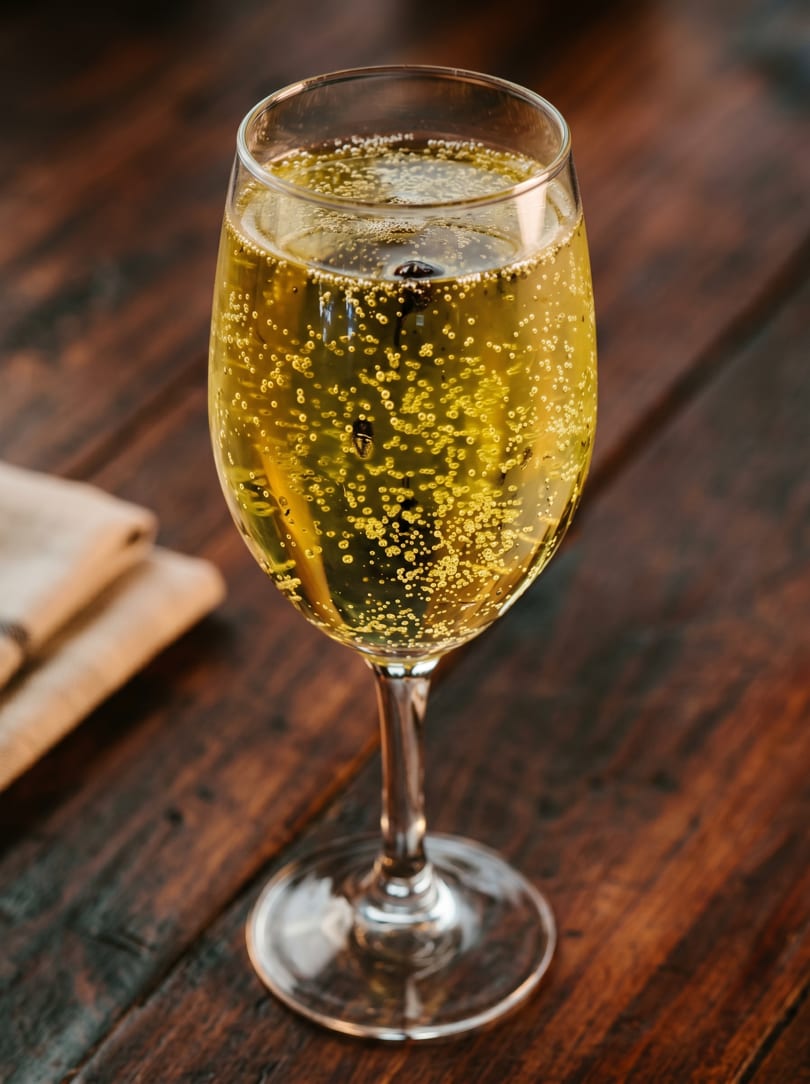 A champagne flute filled with sparkling golden liquid and bubbles on a dark wooden table.