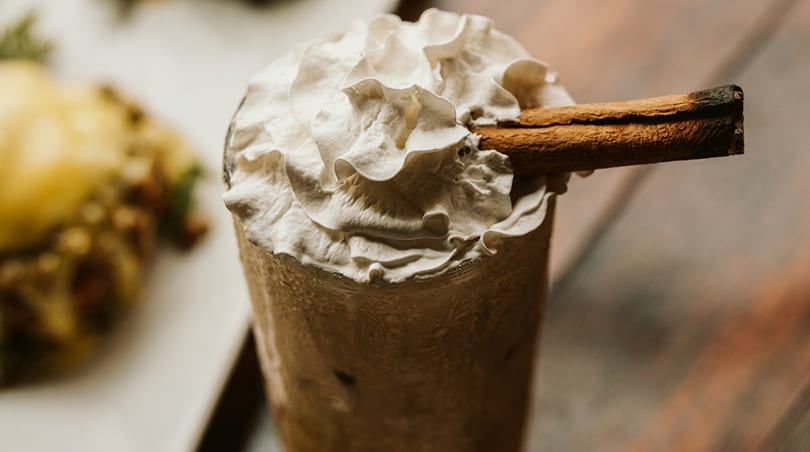Close-up of a creamy beverage topped with whipped cream and a cinnamon stick.